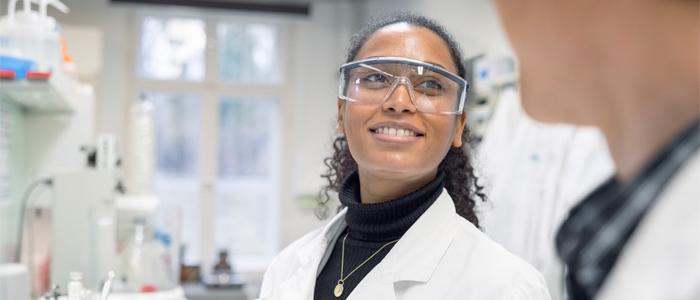 A Black female researcher smiles in a lab. 