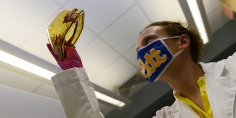 A researcher wearing a face mask examines a specimen. 