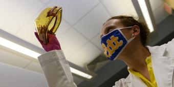 A researcher wearing a face mask examines a specimen.